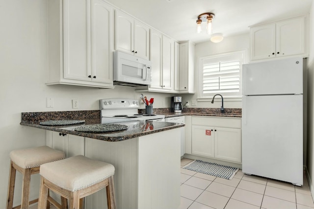 kitchen featuring a breakfast bar area, white appliances, a sink, white cabinets, and dark stone countertops