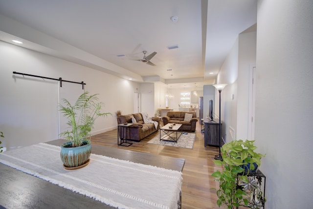 living area featuring ceiling fan, light wood finished floors, a barn door, and baseboards