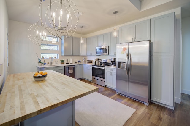 kitchen featuring stainless steel appliances, wooden counters, an inviting chandelier, dark wood-type flooring, and a sink