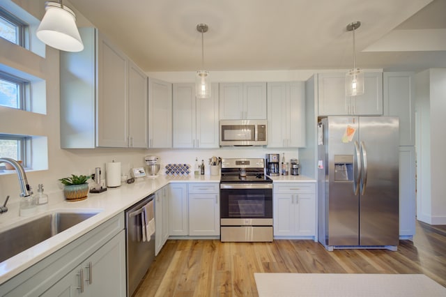 kitchen featuring appliances with stainless steel finishes, light countertops, light wood-style floors, pendant lighting, and a sink