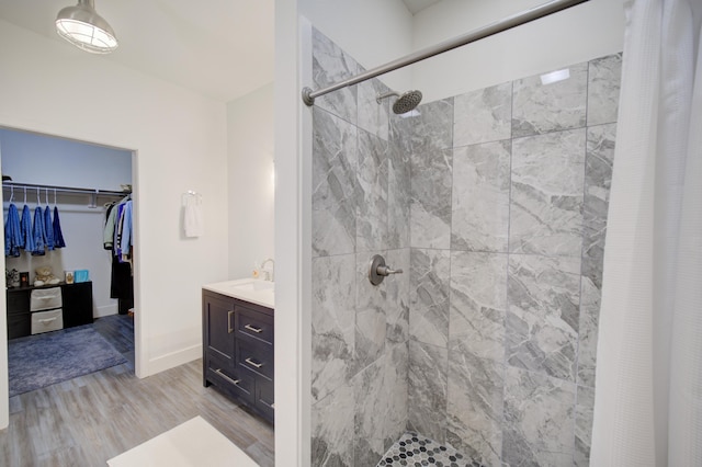 bathroom with a spacious closet, tiled shower, wood finished floors, and vanity