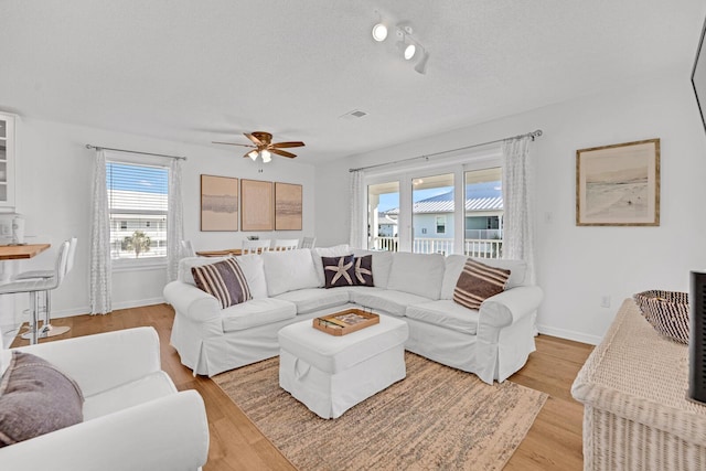 living room featuring ceiling fan, light wood-type flooring, and a textured ceiling