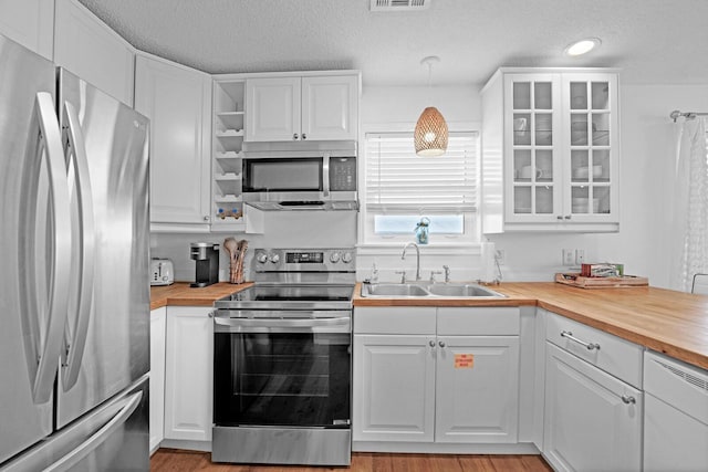 kitchen featuring hanging light fixtures, white cabinetry, stainless steel appliances, and butcher block countertops