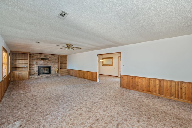 unfurnished living room with a textured ceiling, wood walls, visible vents, wainscoting, and a brick fireplace