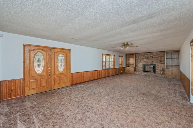 foyer entrance with wainscoting, carpet, a textured ceiling, wood walls, and a brick fireplace