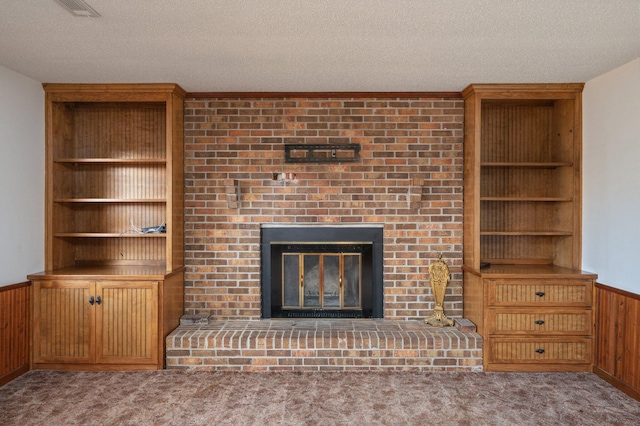 unfurnished living room featuring a wainscoted wall, a textured ceiling, a brick fireplace, and light colored carpet