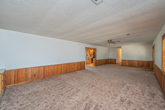 empty room featuring a wainscoted wall, a textured ceiling, a ceiling fan, and wood walls