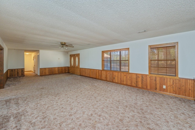 carpeted spare room with wainscoting, wooden walls, and a textured ceiling