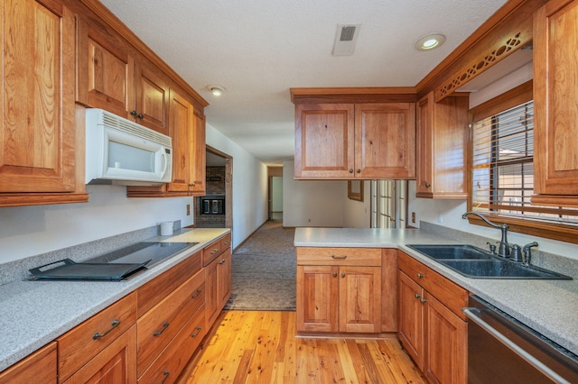 kitchen featuring white microwave, a sink, light countertops, brown cabinets, and dishwasher