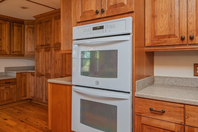 kitchen featuring double oven, brown cabinetry, and light countertops