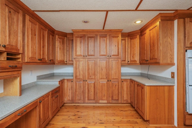 kitchen with a textured ceiling, recessed lighting, light wood-type flooring, and brown cabinets