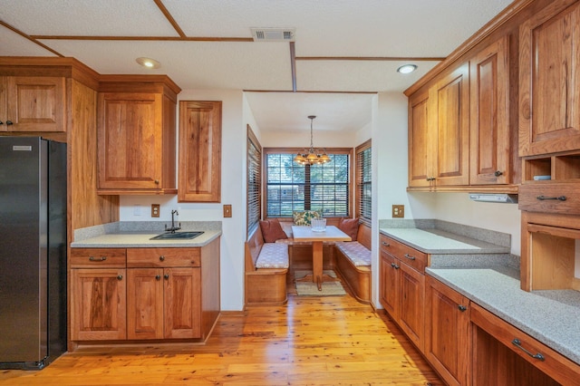 kitchen with visible vents, brown cabinetry, freestanding refrigerator, light wood-type flooring, and a sink