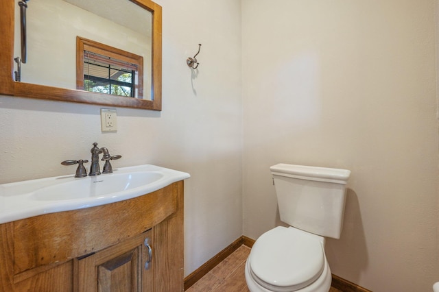 half bathroom featuring toilet, baseboards, wood finished floors, and vanity