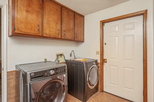 laundry room with cabinet space, light wood-style floors, a textured ceiling, and independent washer and dryer