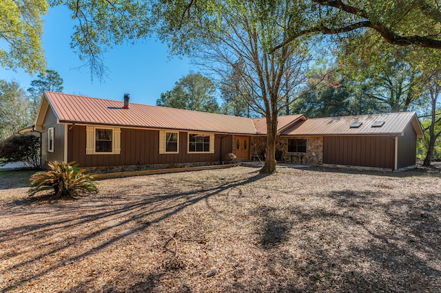 ranch-style home featuring metal roof, driveway, and stone siding