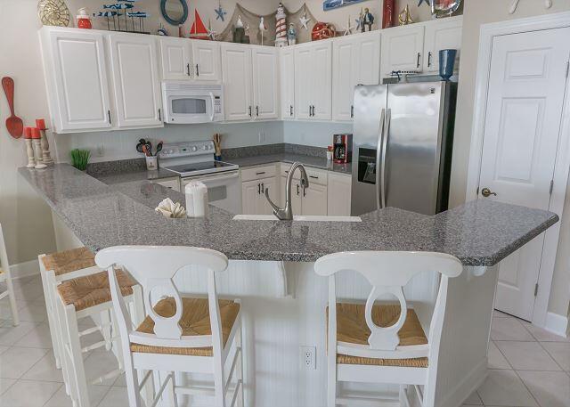 kitchen with light tile patterned floors, white appliances, white cabinetry, a kitchen breakfast bar, and dark stone counters