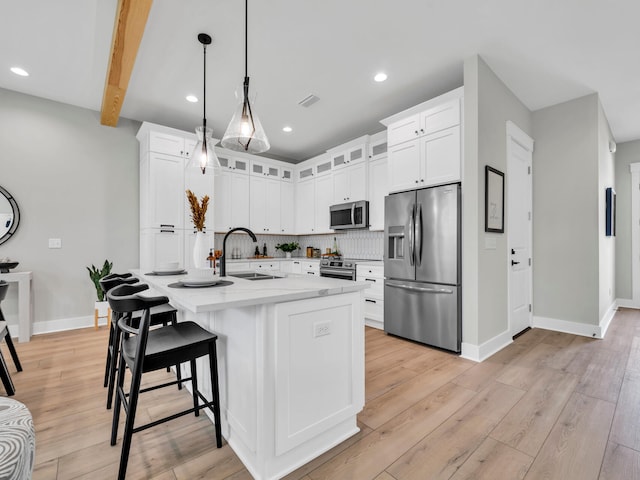 kitchen with appliances with stainless steel finishes, a center island with sink, hanging light fixtures, backsplash, and sink