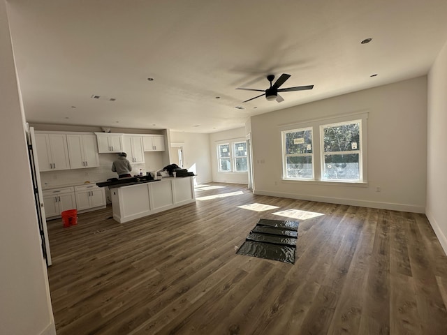 unfurnished living room featuring ceiling fan, baseboards, and dark wood-style floors