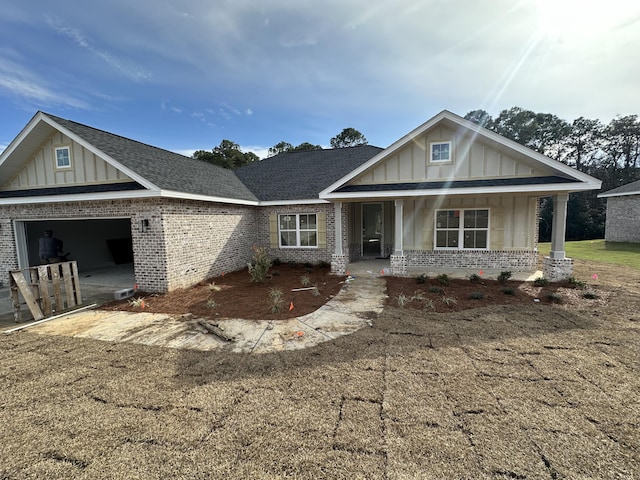 craftsman inspired home featuring board and batten siding, covered porch, a shingled roof, a garage, and brick siding