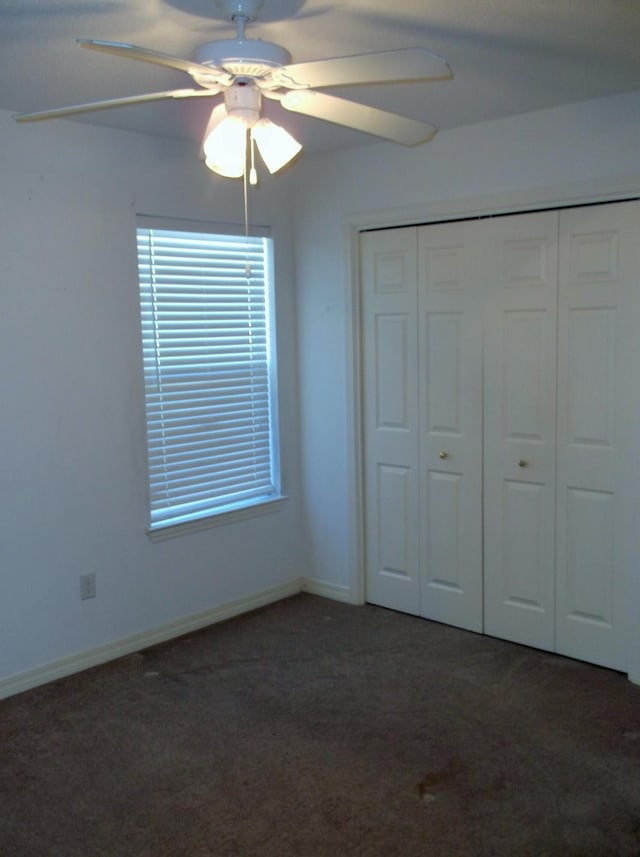 unfurnished bedroom with ceiling fan, dark colored carpet, and a closet