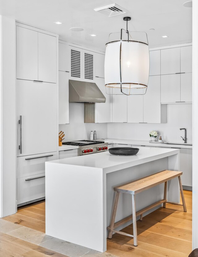 290 Sea Garden St Unit 402, Alys Beach, FL 32461 - kitchen featuring wall chimney exhaust hood, stainless steel gas cooktop, decorative light fixtures, light wood-type flooring, and white cabinetry