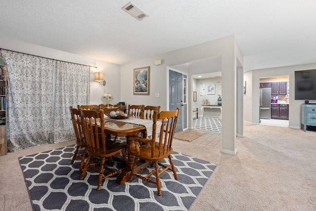 dining room with a textured ceiling, baseboards, visible vents, and light colored carpet