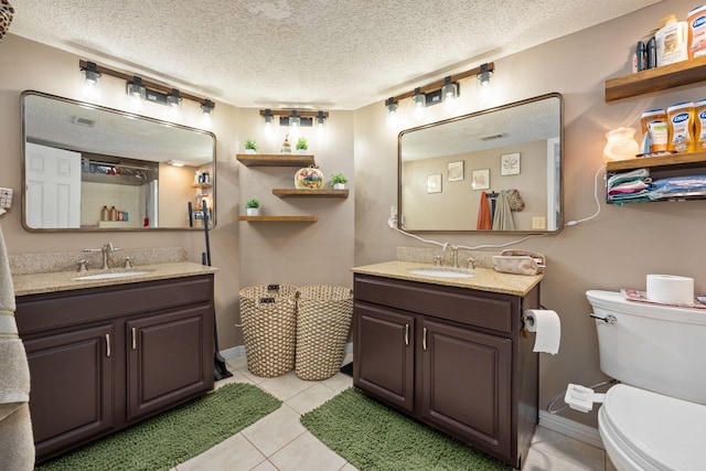 bathroom with toilet, a textured ceiling, two vanities, and a sink