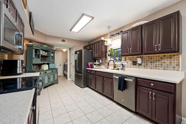 kitchen featuring decorative light fixtures, light countertops, appliances with stainless steel finishes, a sink, and independent washer and dryer