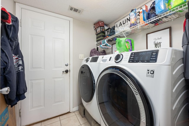 clothes washing area with laundry area, light tile patterned floors, visible vents, washing machine and clothes dryer, and a textured ceiling