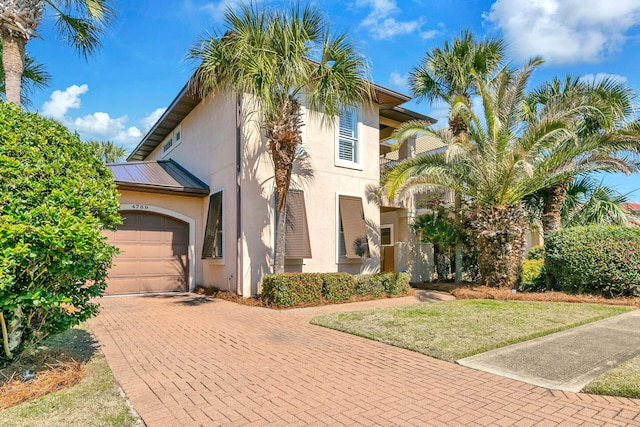 mediterranean / spanish home with metal roof, an attached garage, decorative driveway, stucco siding, and a front lawn