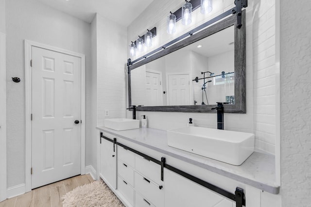 bathroom with double vanity, a shower stall, a sink, and wood finished floors