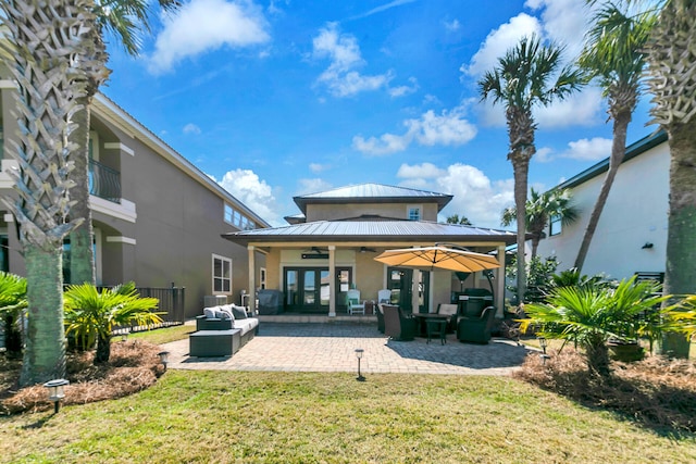 rear view of property with metal roof, a ceiling fan, a lawn, stucco siding, and a standing seam roof