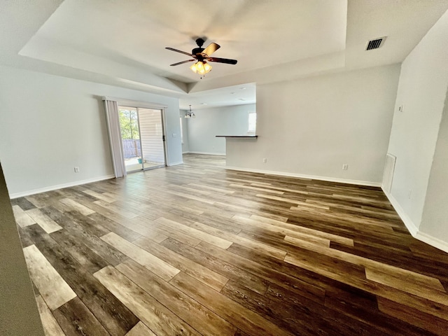 unfurnished room featuring ceiling fan, wood finished floors, a raised ceiling, and baseboards