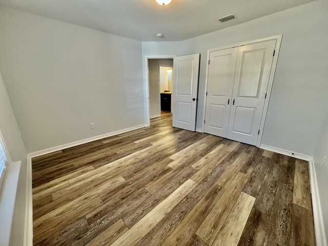 unfurnished bedroom featuring a closet, wood finished floors, visible vents, and baseboards