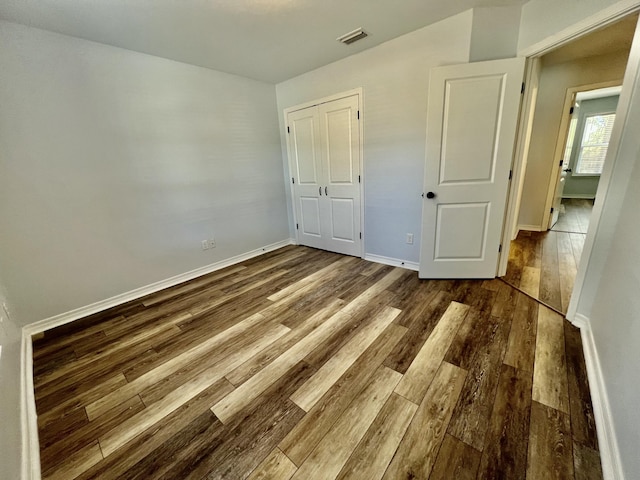 unfurnished bedroom featuring visible vents, a closet, baseboards, and wood finished floors