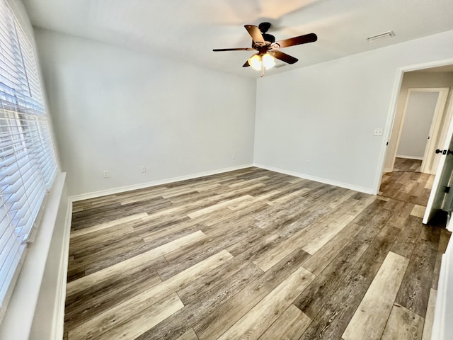 empty room featuring visible vents, wood finished floors, a ceiling fan, and baseboards