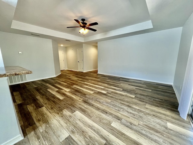 unfurnished living room with baseboards, a tray ceiling, ceiling fan, and wood finished floors