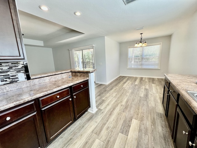 kitchen with tasteful backsplash, hanging light fixtures, light wood-style flooring, dark brown cabinetry, and baseboards