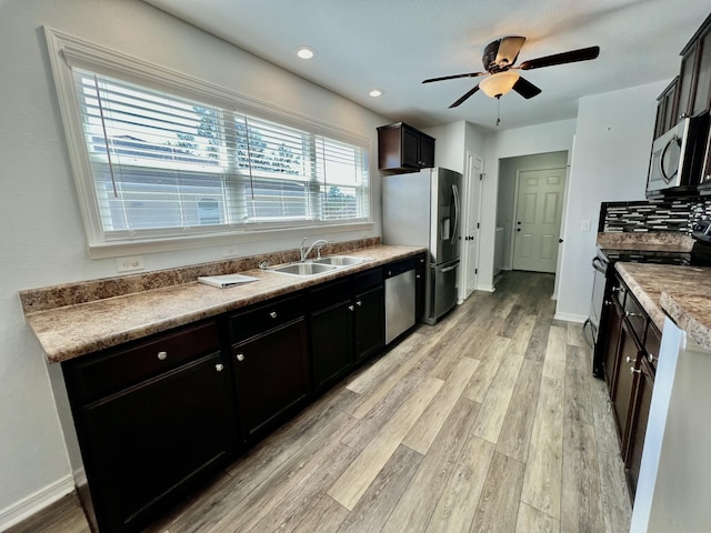 kitchen featuring stainless steel appliances, decorative backsplash, a sink, light wood-type flooring, and baseboards