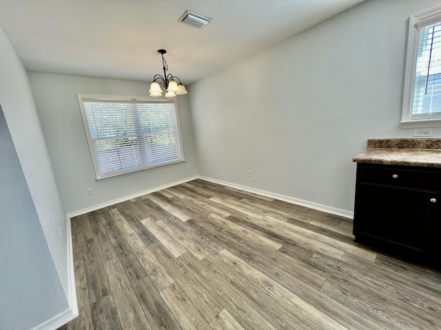 unfurnished dining area featuring a notable chandelier, light wood-style flooring, visible vents, and baseboards