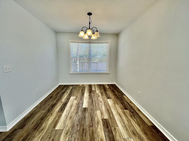 unfurnished dining area featuring a notable chandelier, baseboards, and wood finished floors