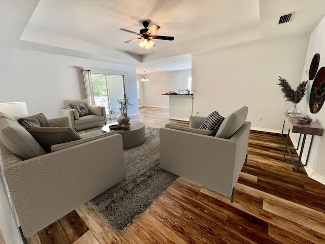 living room featuring dark wood-style floors, a raised ceiling, visible vents, and baseboards