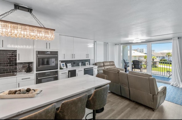 kitchen featuring tasteful backsplash, double wall oven, white cabinets, decorative light fixtures, and light wood-type flooring