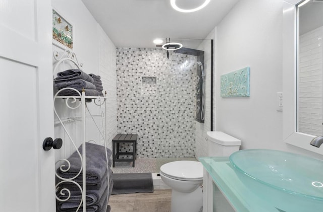 bathroom featuring hardwood / wood-style flooring, vanity, a tile shower, and toilet