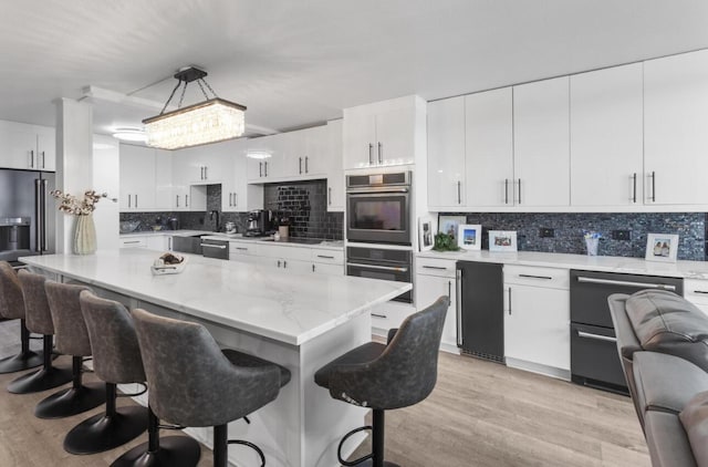 kitchen featuring a kitchen breakfast bar, pendant lighting, black appliances, and white cabinets