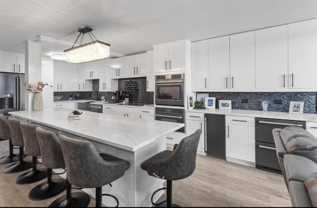 kitchen with double wall oven, decorative light fixtures, decorative backsplash, a breakfast bar, and white cabinetry