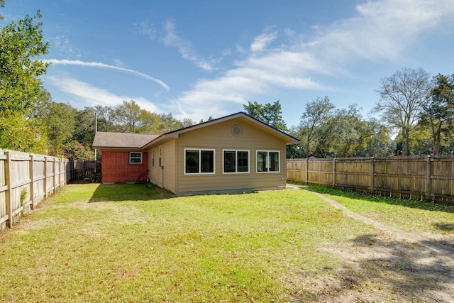 back of house featuring a fenced backyard, a yard, and brick siding