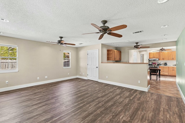 unfurnished living room featuring visible vents, a textured ceiling, baseboards, and wood finished floors