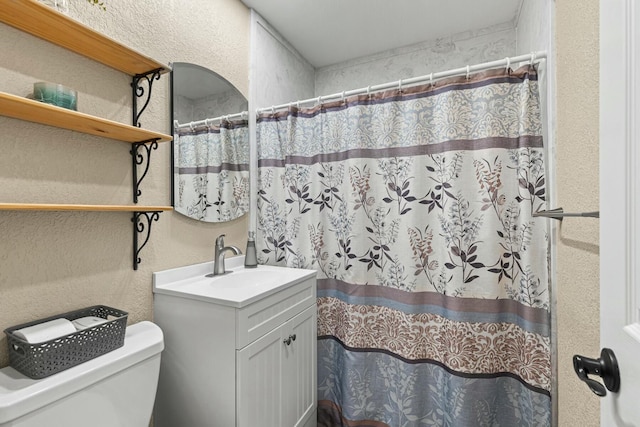 bathroom featuring toilet, a textured wall, a shower with curtain, and vanity