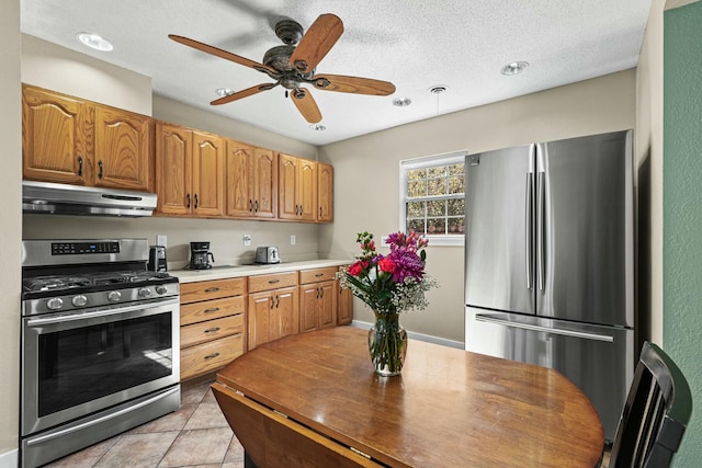 kitchen featuring a textured ceiling, light tile patterned flooring, under cabinet range hood, stainless steel appliances, and light countertops